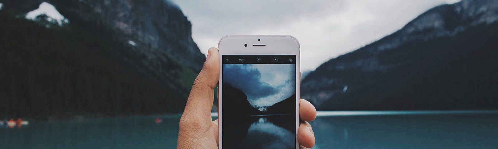 iPhone in a man’s hand, pointing at a beautiful lake