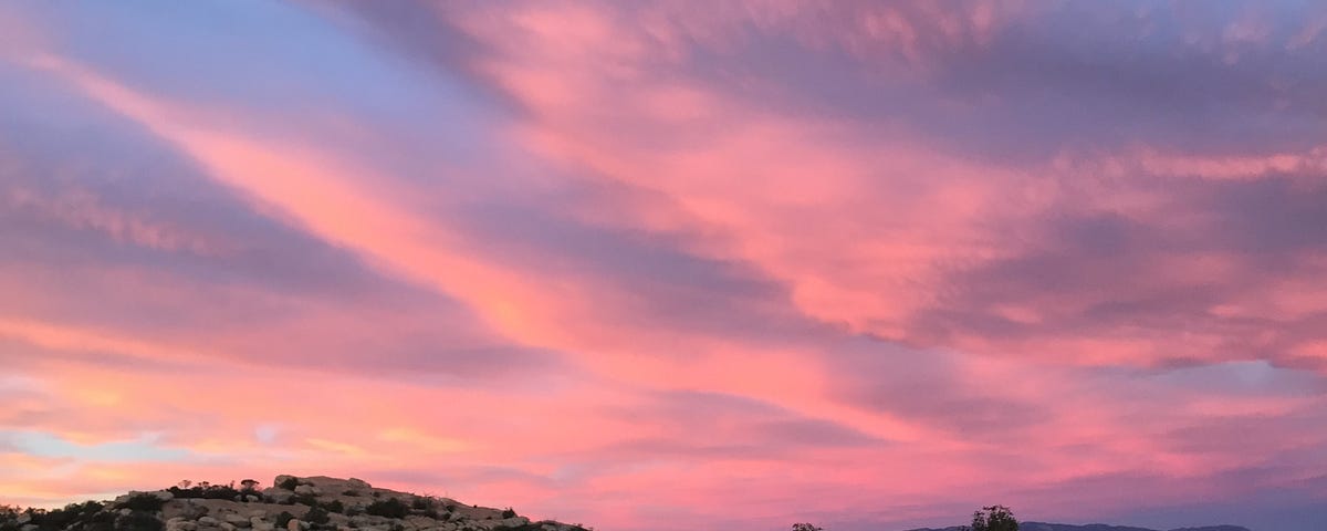 A sky shown at sunset, with pink clouds hanging over a rocky area.