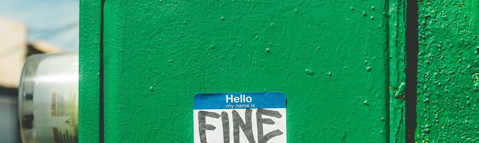 Image of green electric meter outside of building with a name tag sticker “Hello my name is” with the word “FINE” in black sharpie.