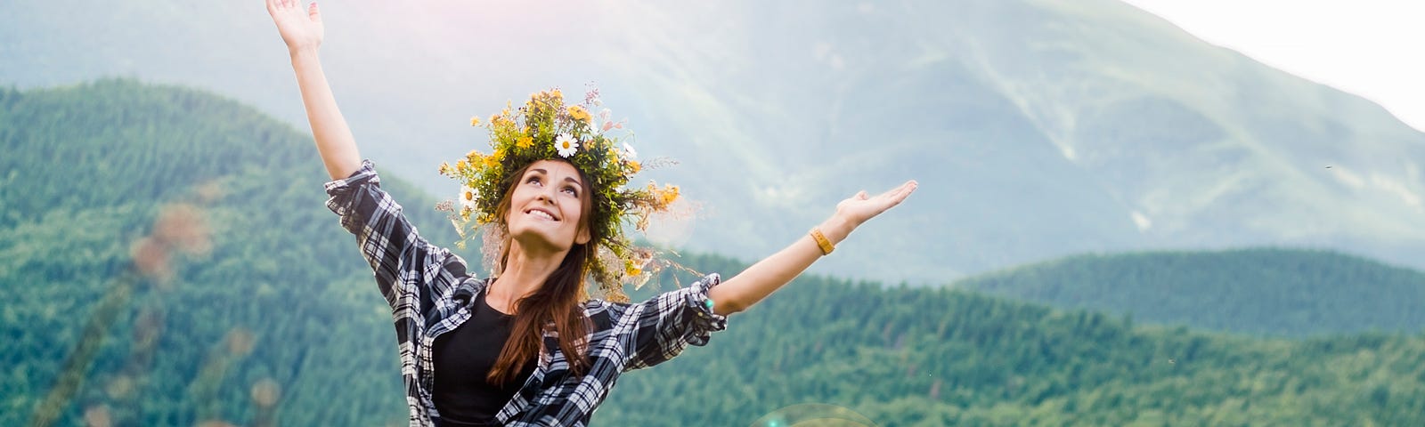 Joyous woman with flowers in her hair, arms outstretched in a mountain meadow!