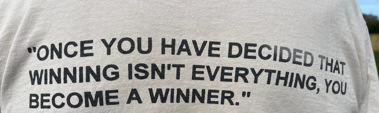 The back of a man in a t-shirt, bearing the quote “Once you have decided that winning isn’t everything, you become a winner.” George Sheehan, M.D. 1918–1993