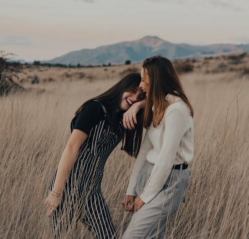 Two girls laughing in a field of tall grass.