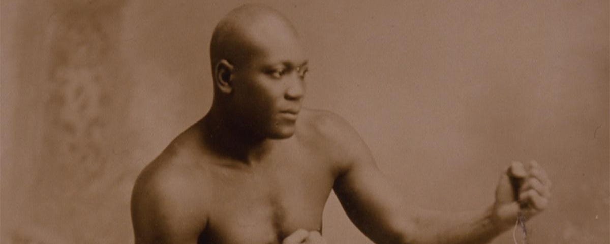 A man with a shaved head and brown skin stands in a boxing stance