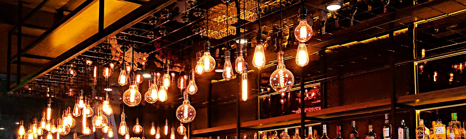 A trendy bar, with rows of bottles on the back wall and exposed lighting overhead.