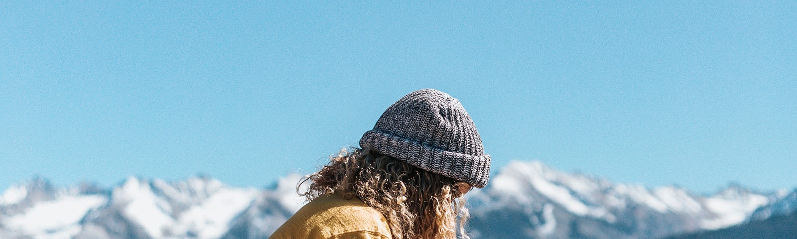 A woman sitting on a rock that is overlooking the snow capped mountain peaks, and writing something on her notebook.