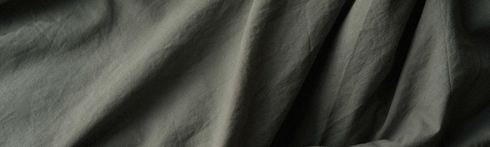 Photo of a grey sheet, draped with uneven folds & bunched in one corner