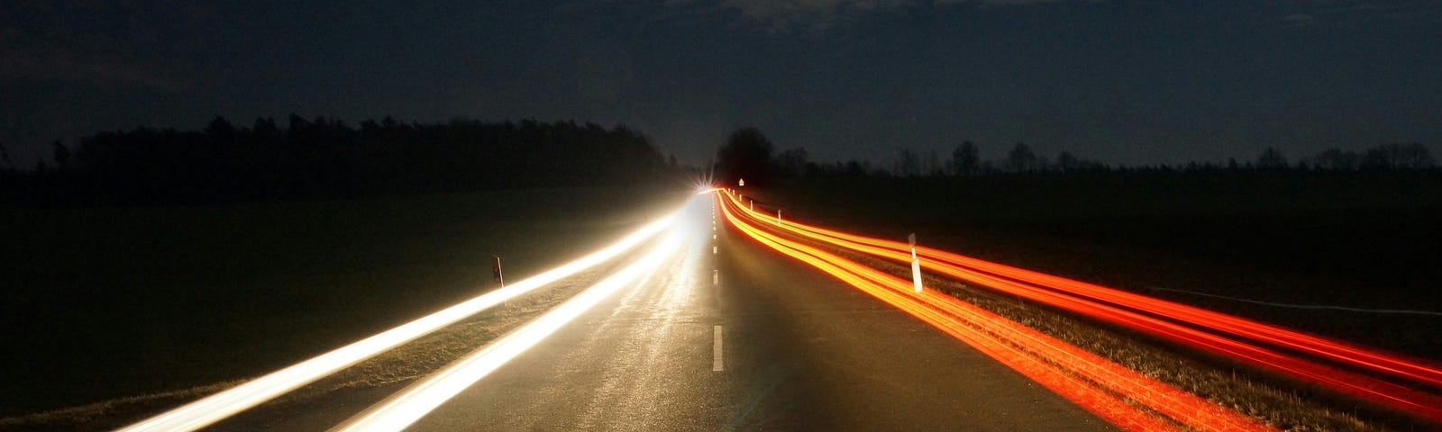 a time-lapse photo looking down a highway and showing the red lines of taillights on one side and the white lines of headlights on the other.