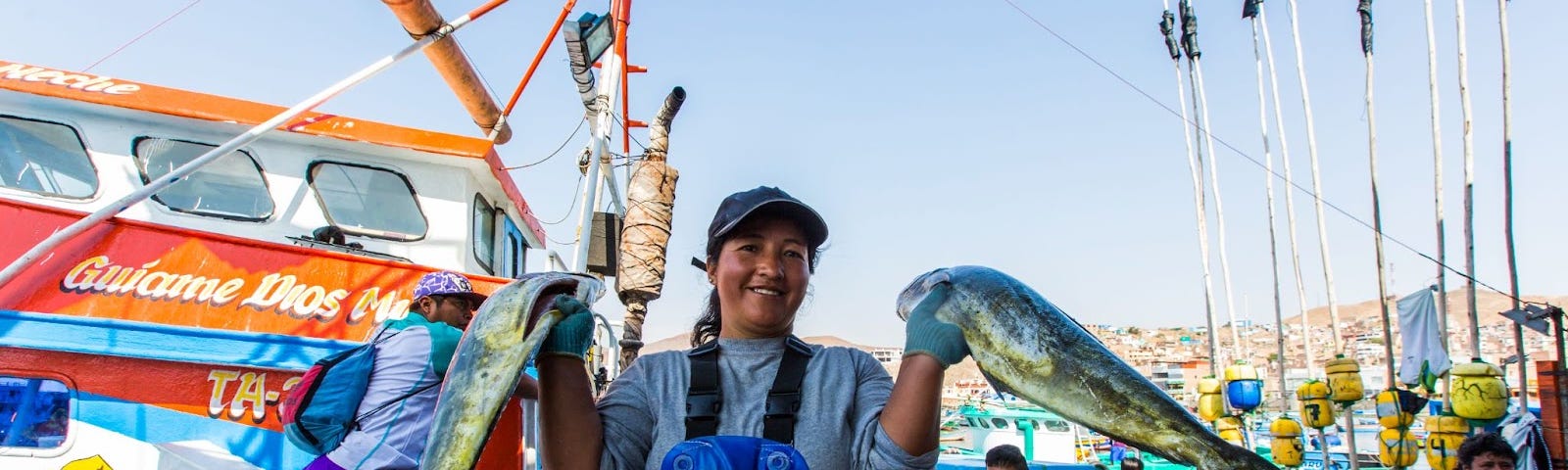 A smiling woman holds two large fish in each hand.