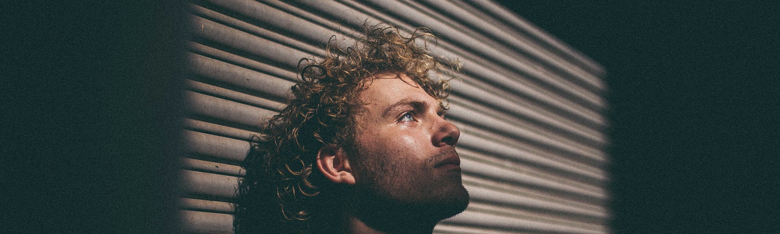 blonde man resting his head against the wall