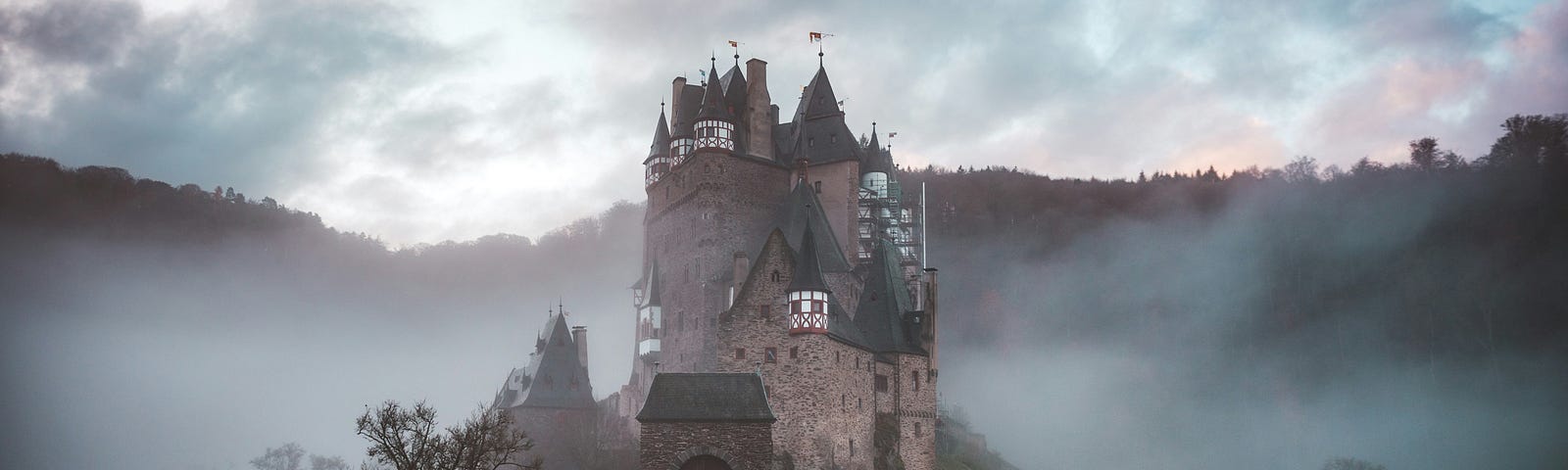 Castle in a hilly landscape surrounded by fog.