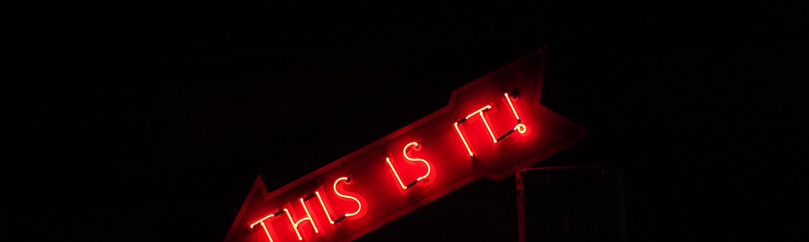 A red neon sign shaped like an arrow with the words, “This is it!” written in capital letters.