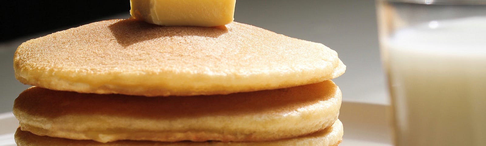 Photo of a stack of pancakes with a glass of milk on the side