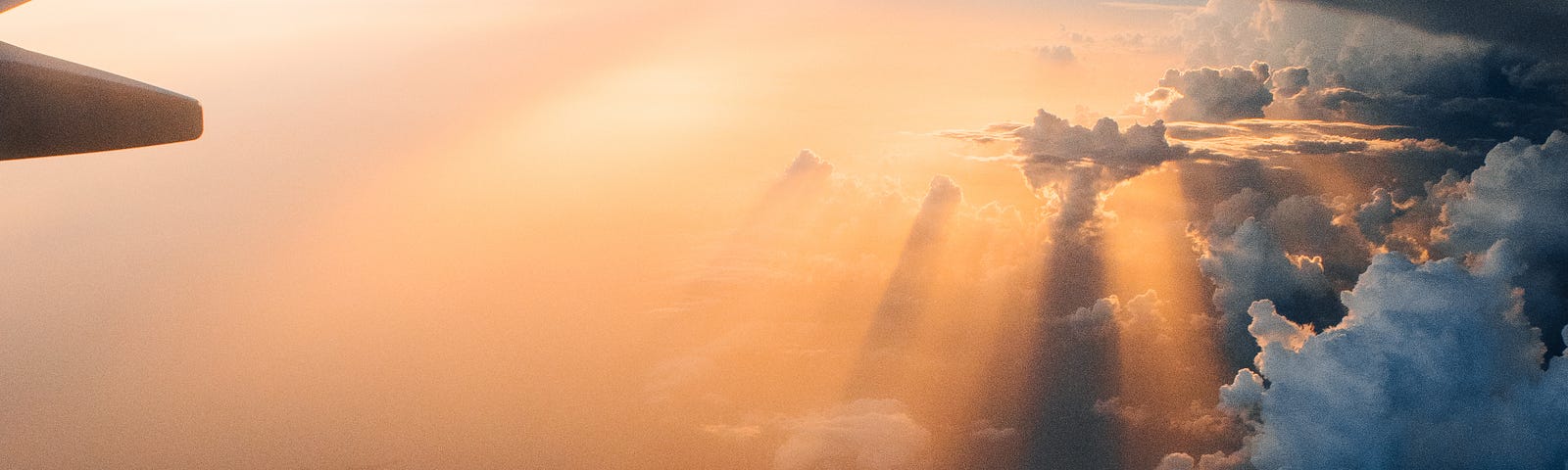 the view out of an aeroplane window, with clouds and rays of orange sunlight coming through