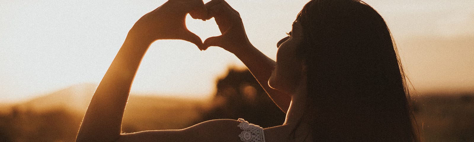 Woman making heart sign at sunset