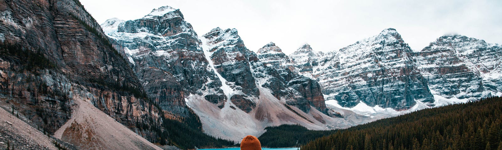 A photo of a person facing and looking at a beautiful landscape of river and mountain.