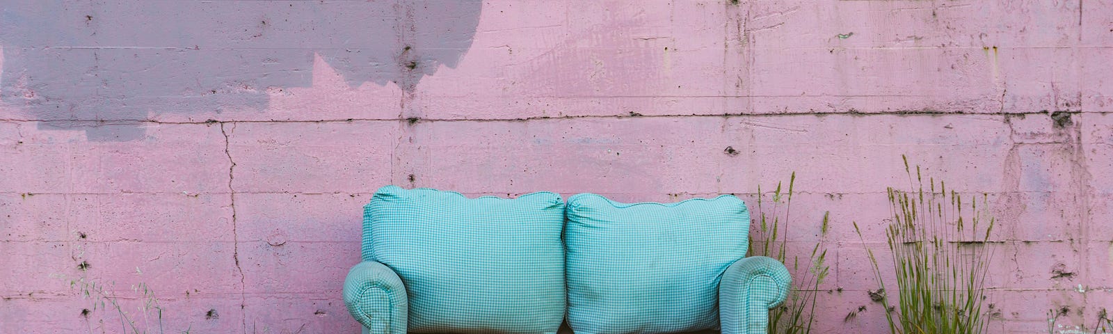An old, broken blue sofa in front of a pink wall