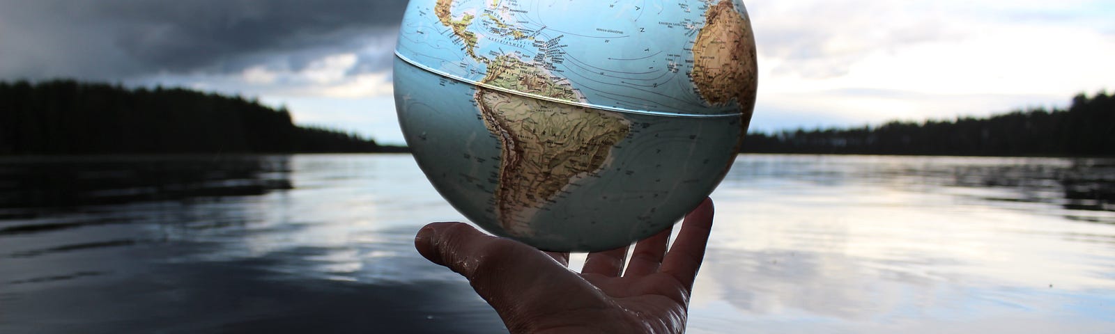 Outstretched hand holding the globe with background of water, trees, and sky