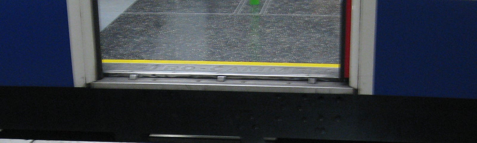 Image of an open door of a subway car with the door a few inches off from the station level and tiles spelling out mind the gap.