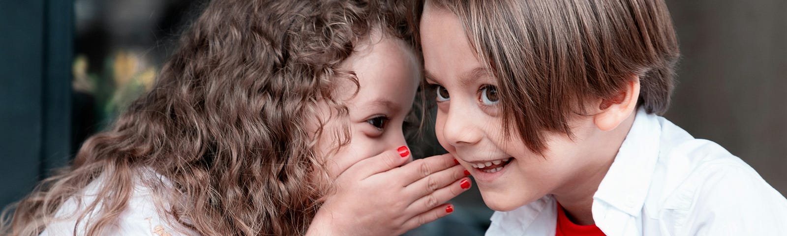 A little girl whispering a secret to a little boy