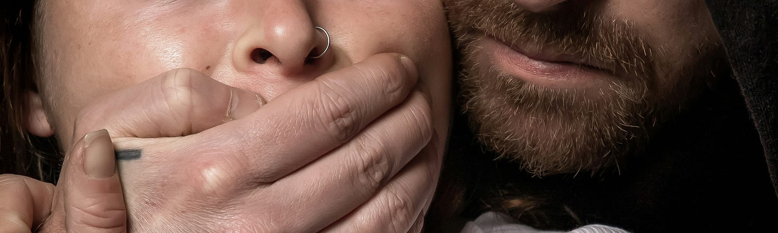 Photo of a man holding his hand across a frightened woman’s face.
