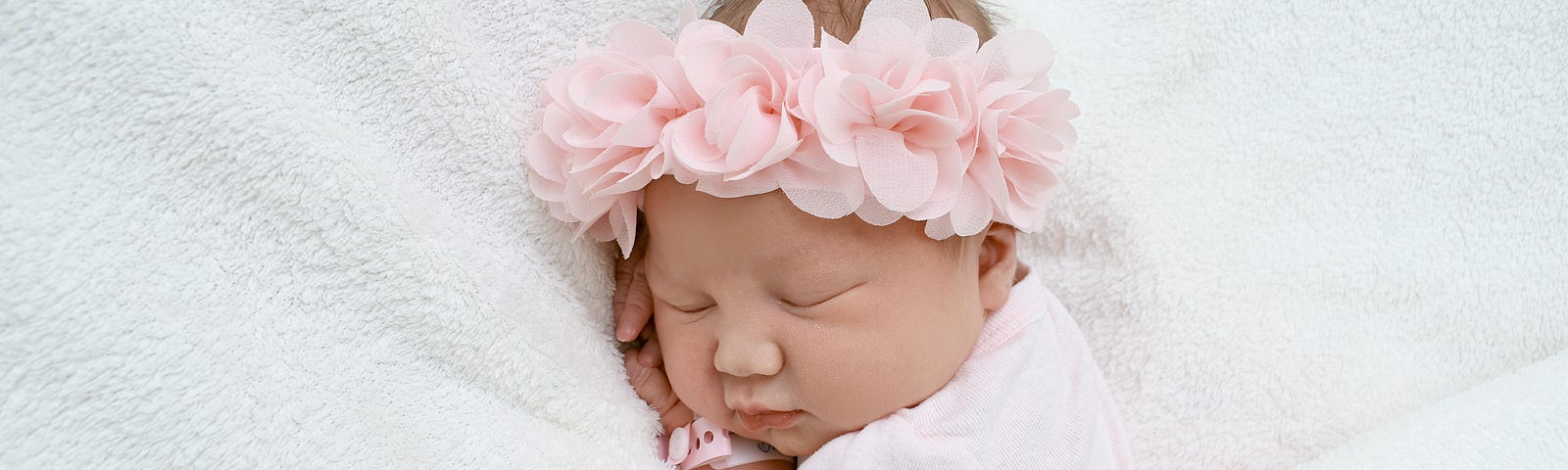New born baby girl lying between white sheets with pink bow in her hair.