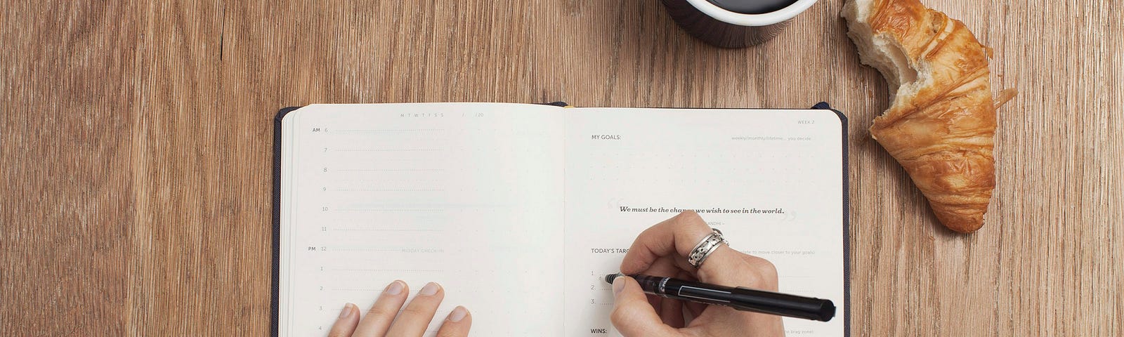 A woman writing in a journal, while eating a croissant and drinking coffee