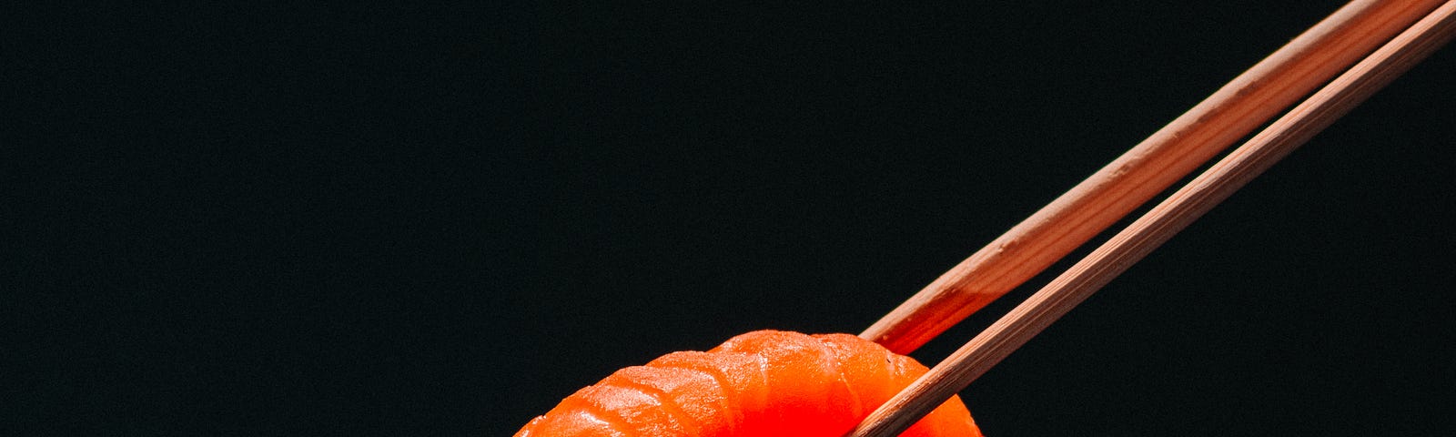 A pair of chopsticks extends from the upper right of the image to grasp a piece of sushi (salmon). Oily fish consumption is associated with a lower risk of chronic kidney disease.