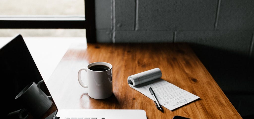 a laptop, smartphone, notebook and coffee mug on a wooden office table