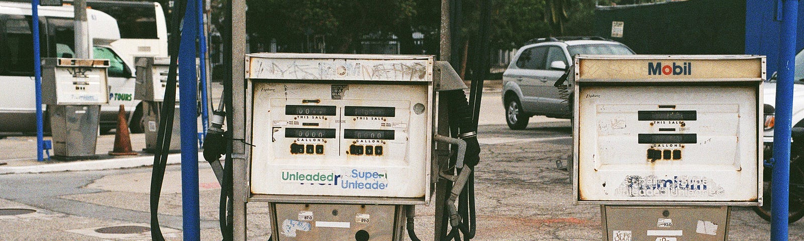 Two aging gas pumps side by side that appear worn and weathered by time