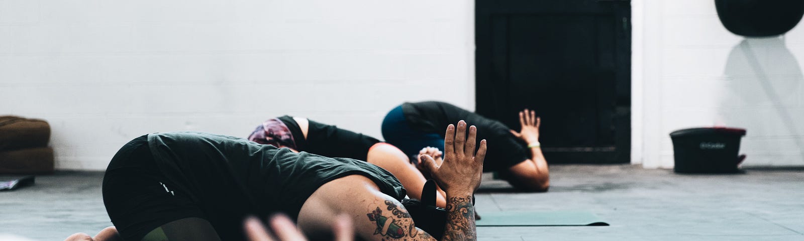 Four yoga students are lined up on their mats, in childs pose, with their elbows bent and hands in prayer position.