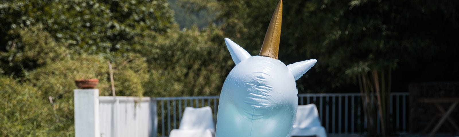 An unknown person riding a large unicorn float in a pool.