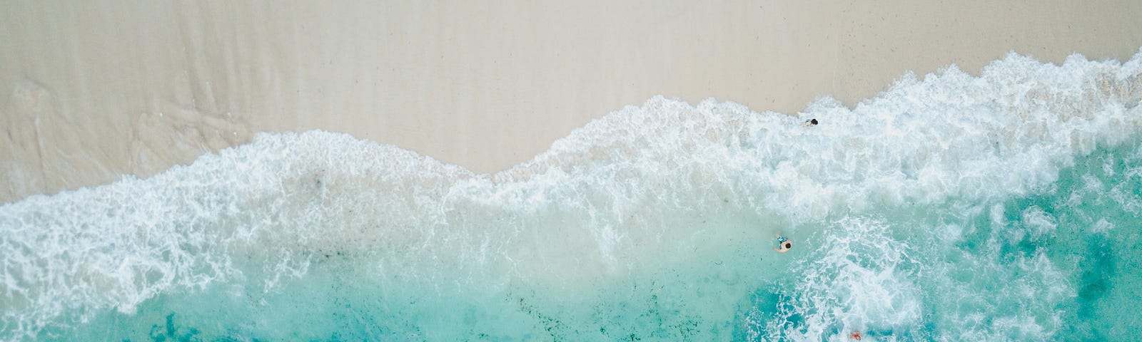 Gods-eye view of rich, blue waves crashing down onto a nearly empty beach.