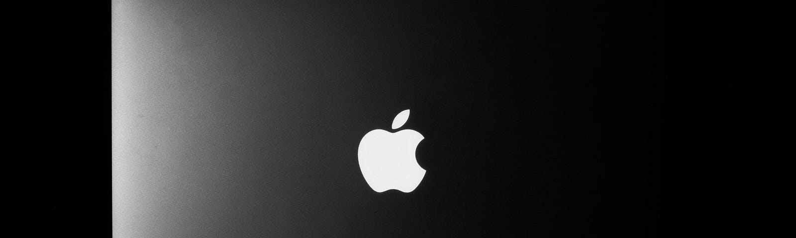 A MacBook on a dark background, Apple logo illuminated