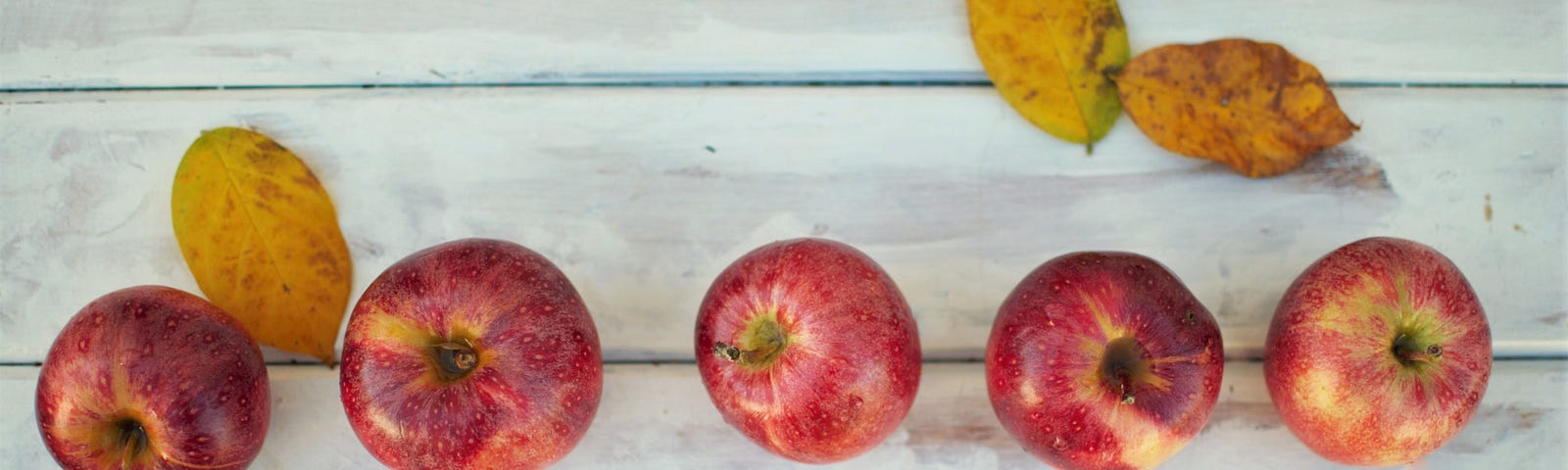 Apples placed in a rather imperfect line, on a white wooden table