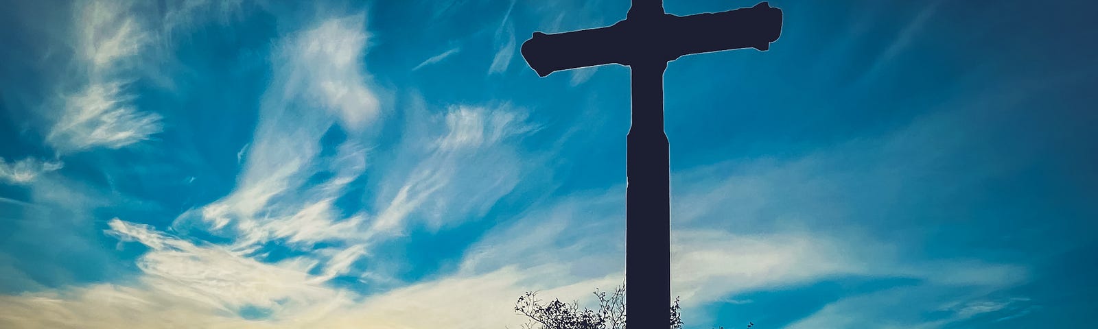 The silouette of a person kneeling at a cross with a blue and yellow sky in the background