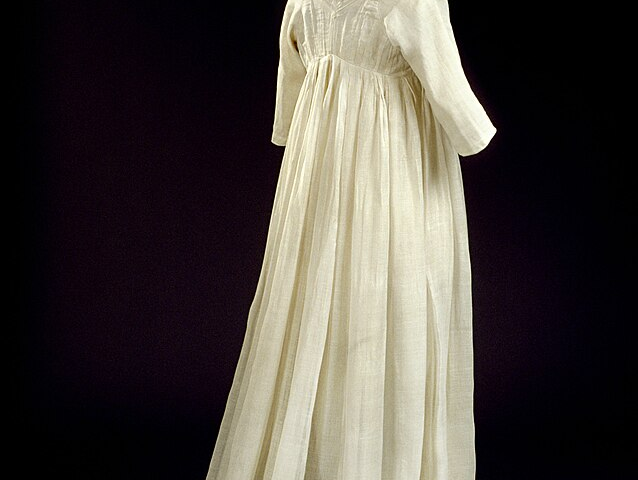 A photograph of a floor length dress, three-quarter sleeves, cream colored dress with embroidered flowers and leaves around the hem.