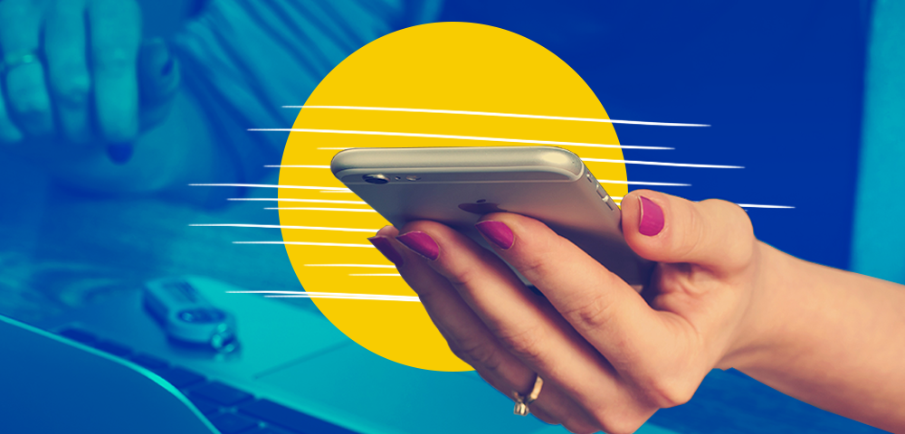 Woman’s hand holding silver iphone in front of yellow circle, with laptop in blue background