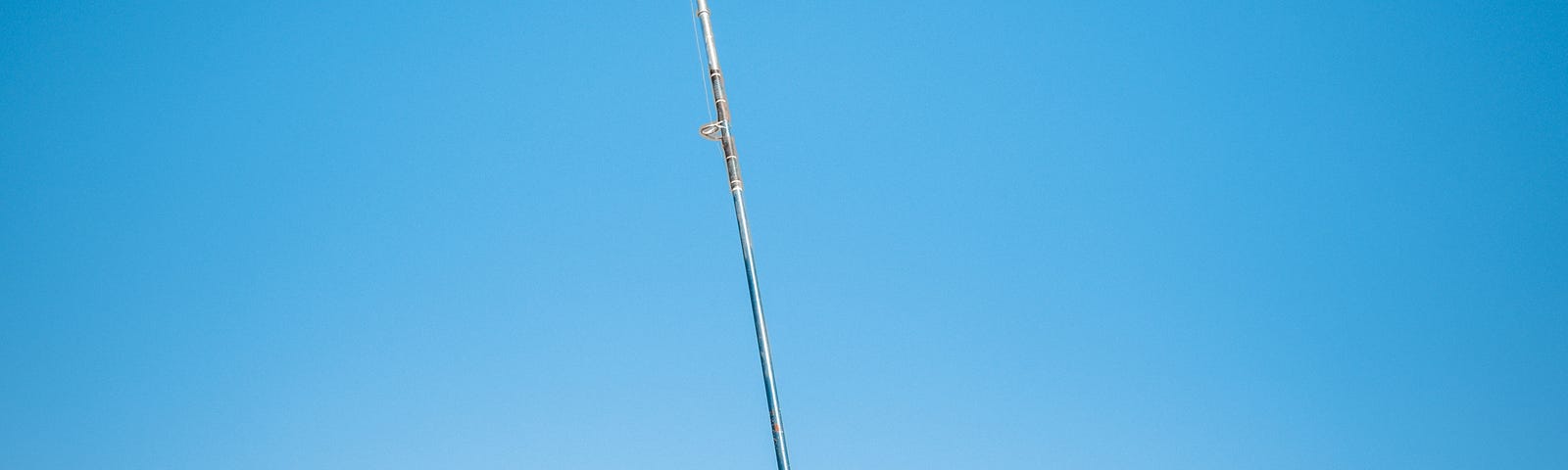 Photo of a bent fishing pole stuck in the sand on the ocean shore.