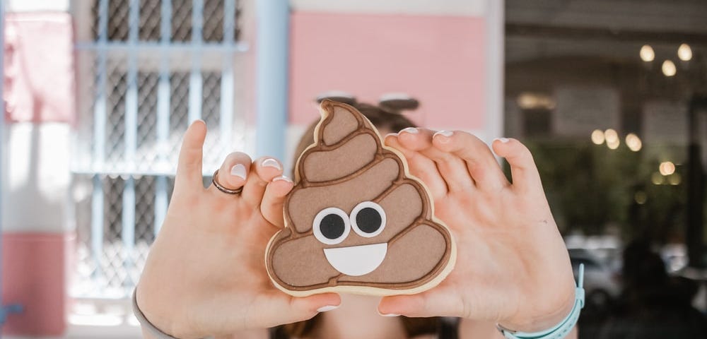 A girl holds a decorated poop emoji-shaped cookie in front of her face