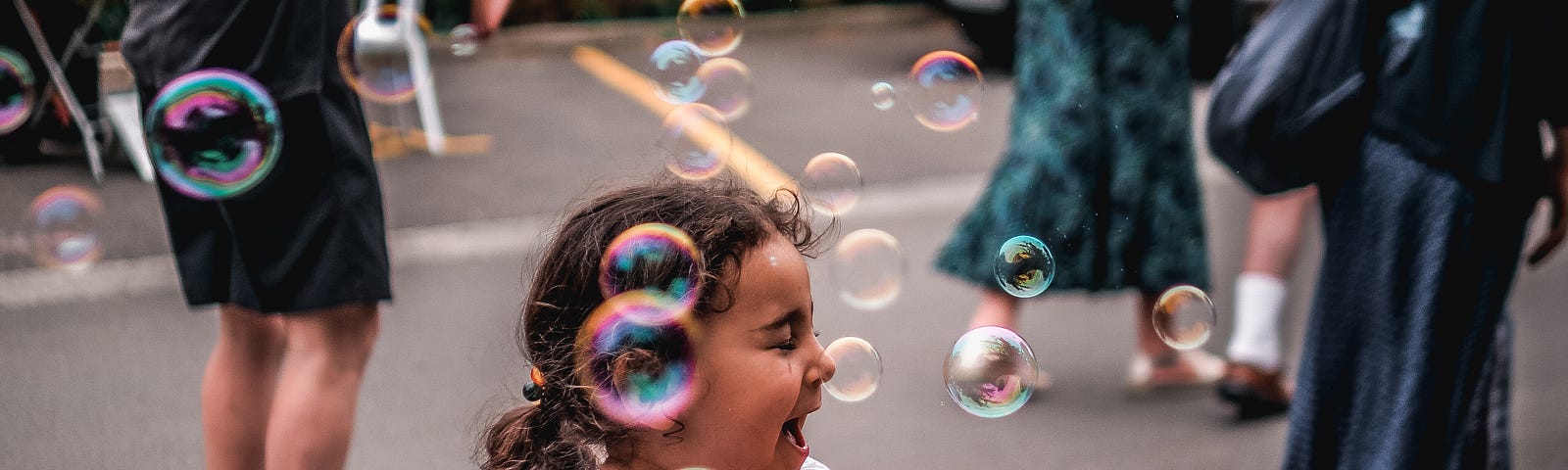 A laughing child on a sidewalk, with soap bubbles around her