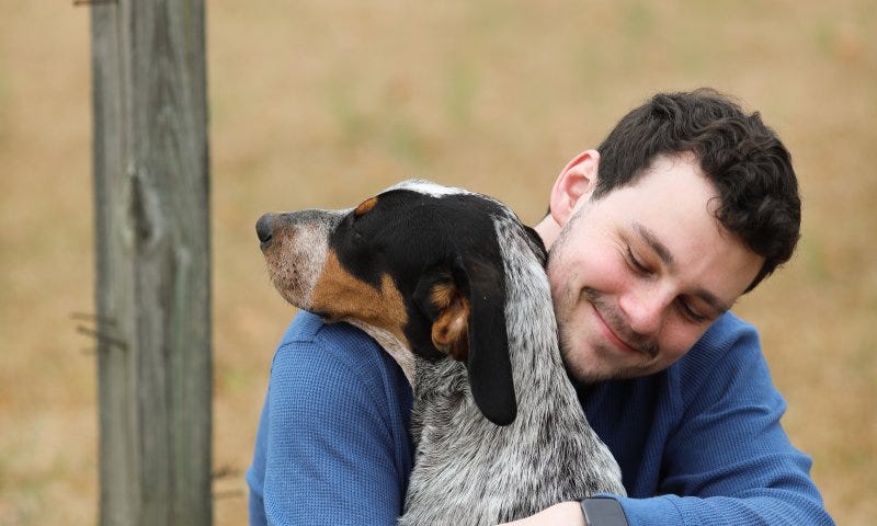 Blue sweater dressed owner hugging his dog with a happy smile face.