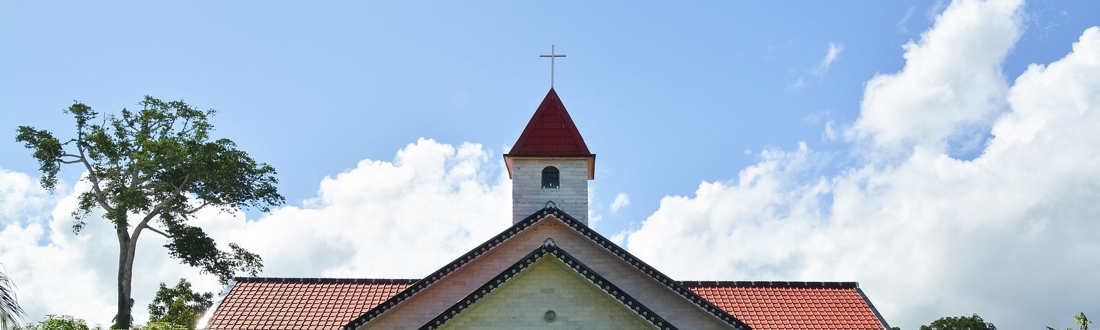 Photo of the exterior of a church building with a steeple and cross.