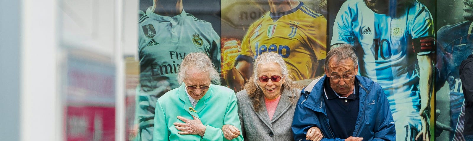 Three elderly folk walking in front of a sports mural