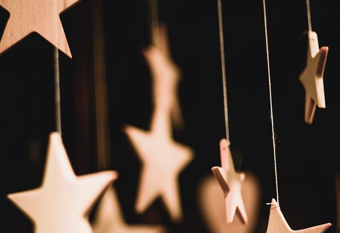 Small, pale wooden stars hanging from thin pieces of twine, against a black background.