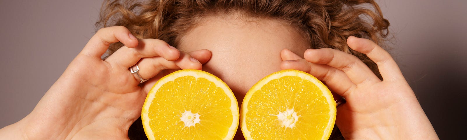 A woman holds two orange slices directly over her eyes.