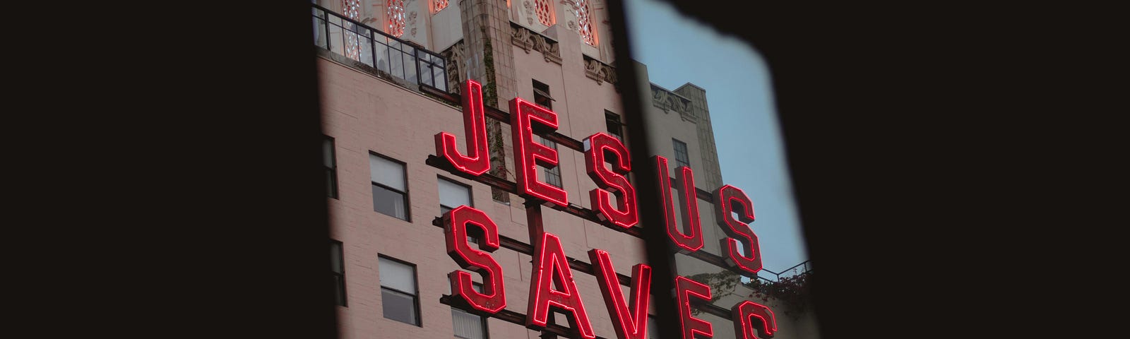 Red sign “Jesus Saves” from a window. With a building in the background.