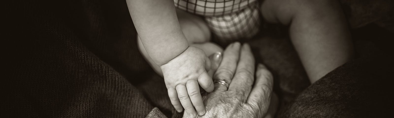 Old woman grabbing a baby’s hand