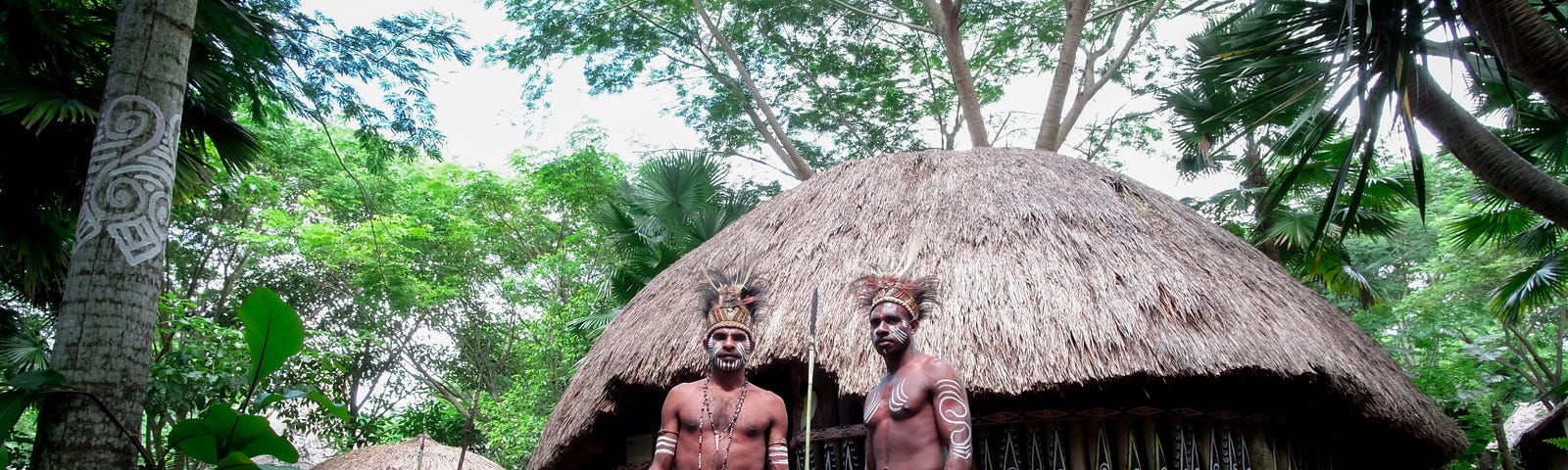 Two Village Men Standing before a hut in the jungle.