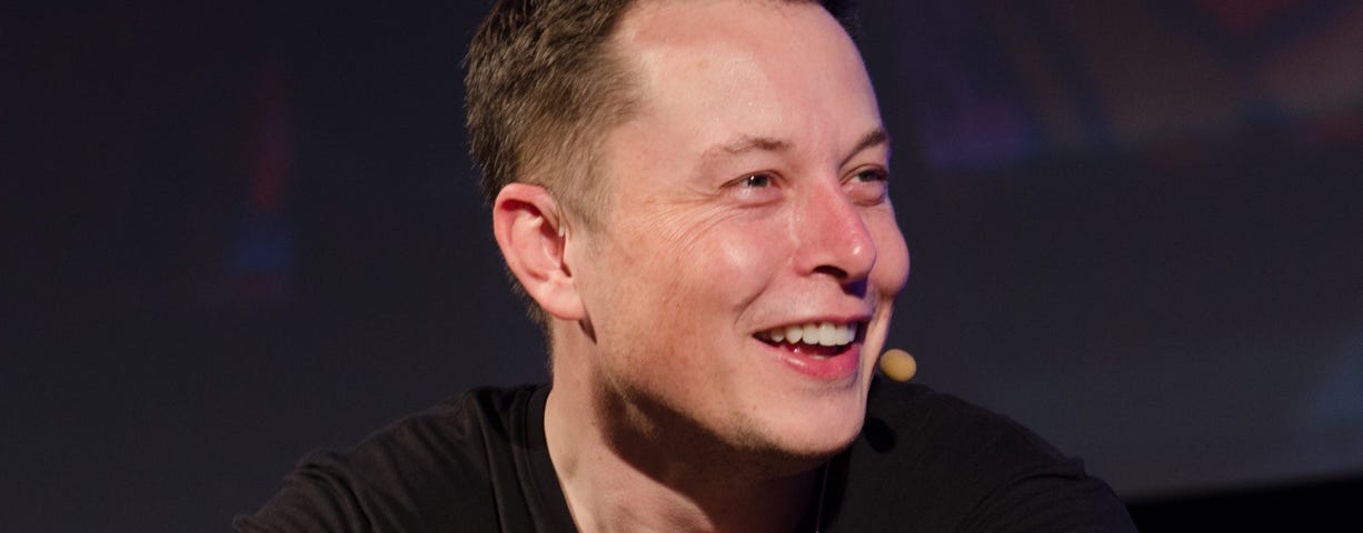 Elon Musk smiling while wearing a microphone