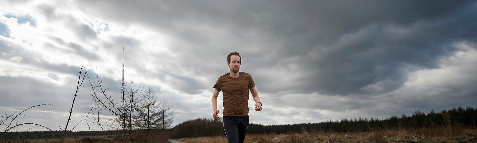 Man running on a dirt road under grey, overcast skies